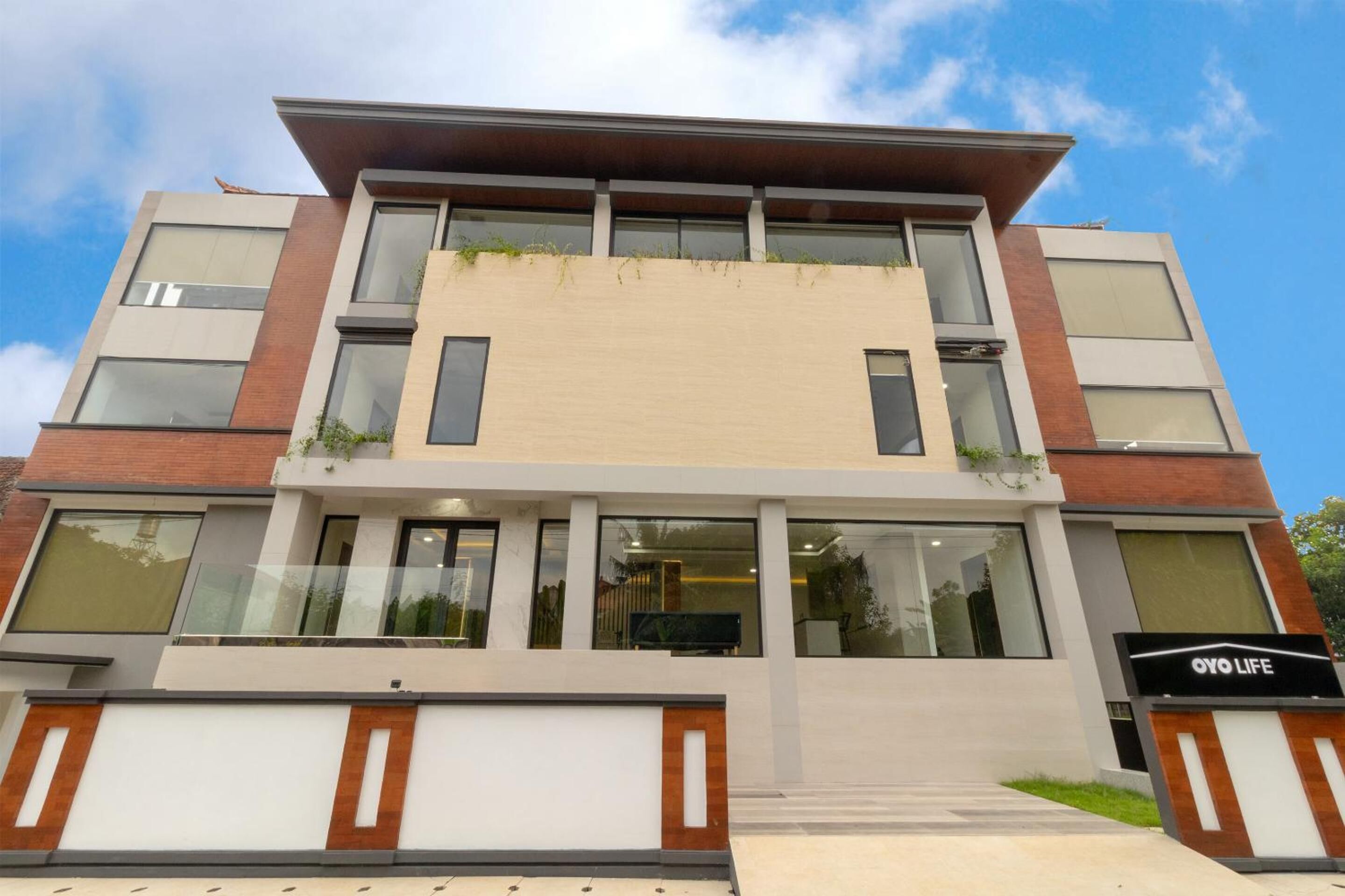 A modern multi-story building with a flat roof, large windows, and a sign reading "OYO LIFE".
