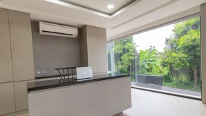 Una cocina moderna con una computadora portátil sobre la encimera, aire acondicionado integrado y un amplio ventanal con vistas a zonas verdes.