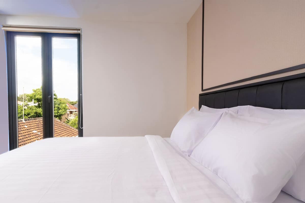 A neatly made bed with white linens in a hotel room with a view of a residential area through a sliding glass door.