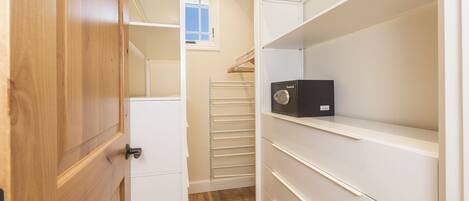 A walk-in closet with wooden doors, white shelving, and a black storage box.