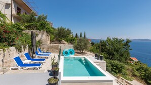 Ein Poolbereich mit blauen Liegestühlen, einem kleinen Pool und Blick aufs Meer.
