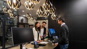 A reception desk with a computer monitor, a phone, and a payment terminal. - Studio+ - HARBR. Hotel Heilbronn (Heilbronn)