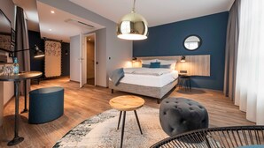 A modern bedroom with a bed, bedside tables, a hanging light fixture, and a round mirror on the wall. - Studio+ - HARBR. Hotel Heilbronn (Heilbronn)