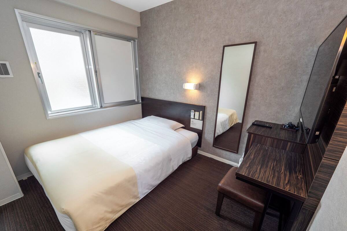 A hotel room with a single bed, a bedside table, a mirror, and a window.
