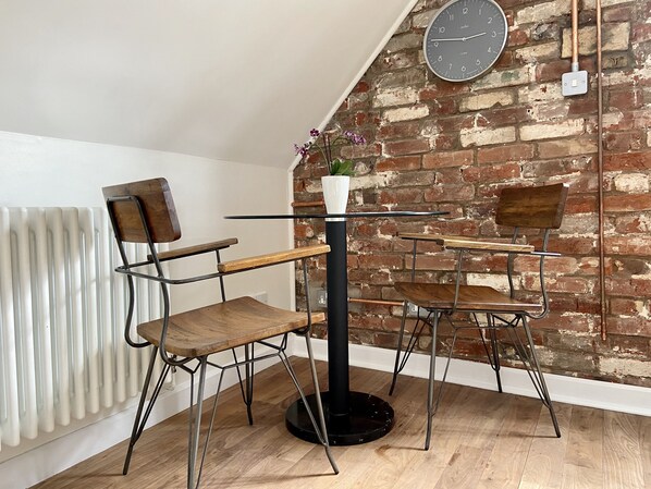 A modern loft-style room with exposed brick walls, a white radiator, and a round table with chairs.