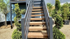 A modern building with a blue exterior, a wooden staircase with metal railings, and surrounding greenery. - A Spacious, Modern & Contemporary Loft Space (Wickham Market)
