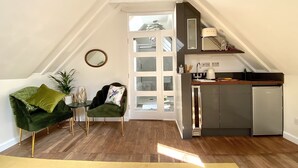 A compact living space with a kitchenette, a green sofa, a chair with a decorative pillow, and a wooden floor. - A Spacious, Modern & Contemporary Loft Space (Wickham Market)
