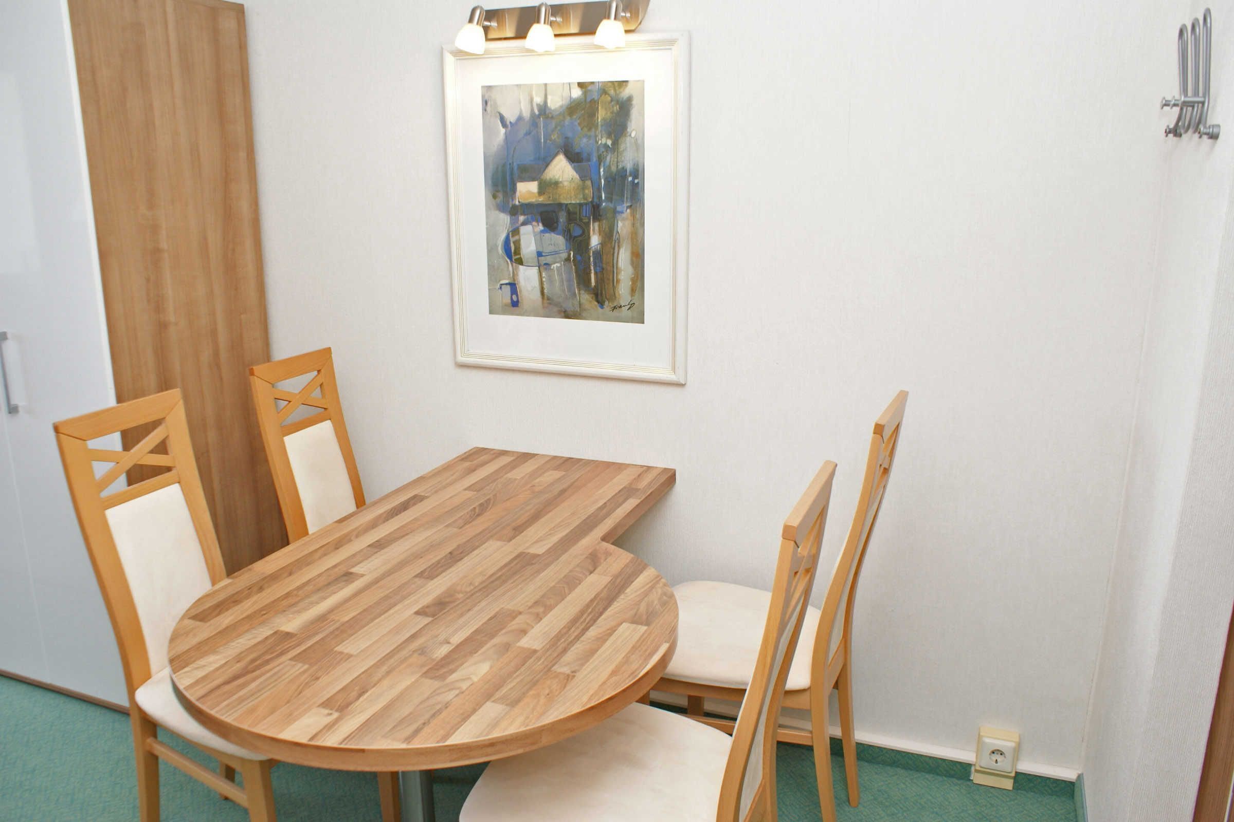Un área de comedor con una mesa redonda de madera y cuatro sillas, un cuadro enmarcado en la pared y una puerta de madera.
