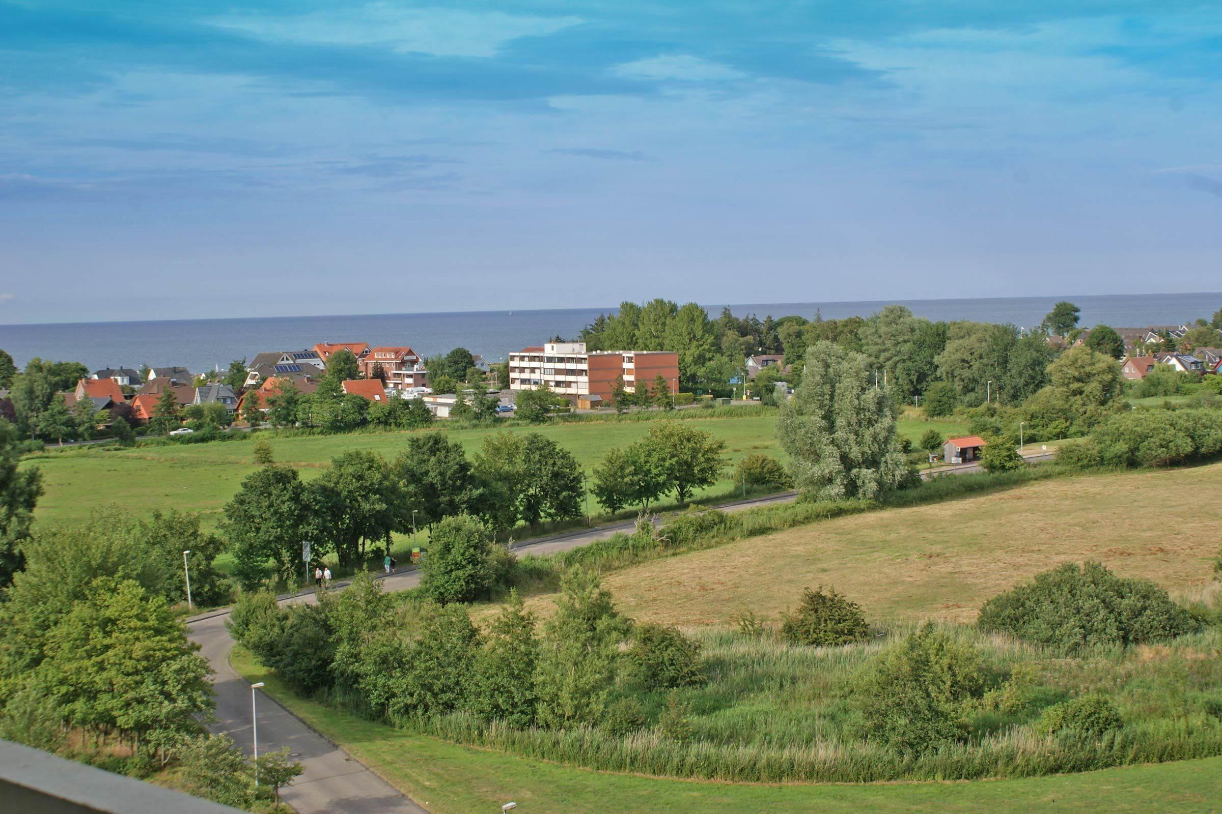 A residential area with houses, a road, and a body of water in the background.