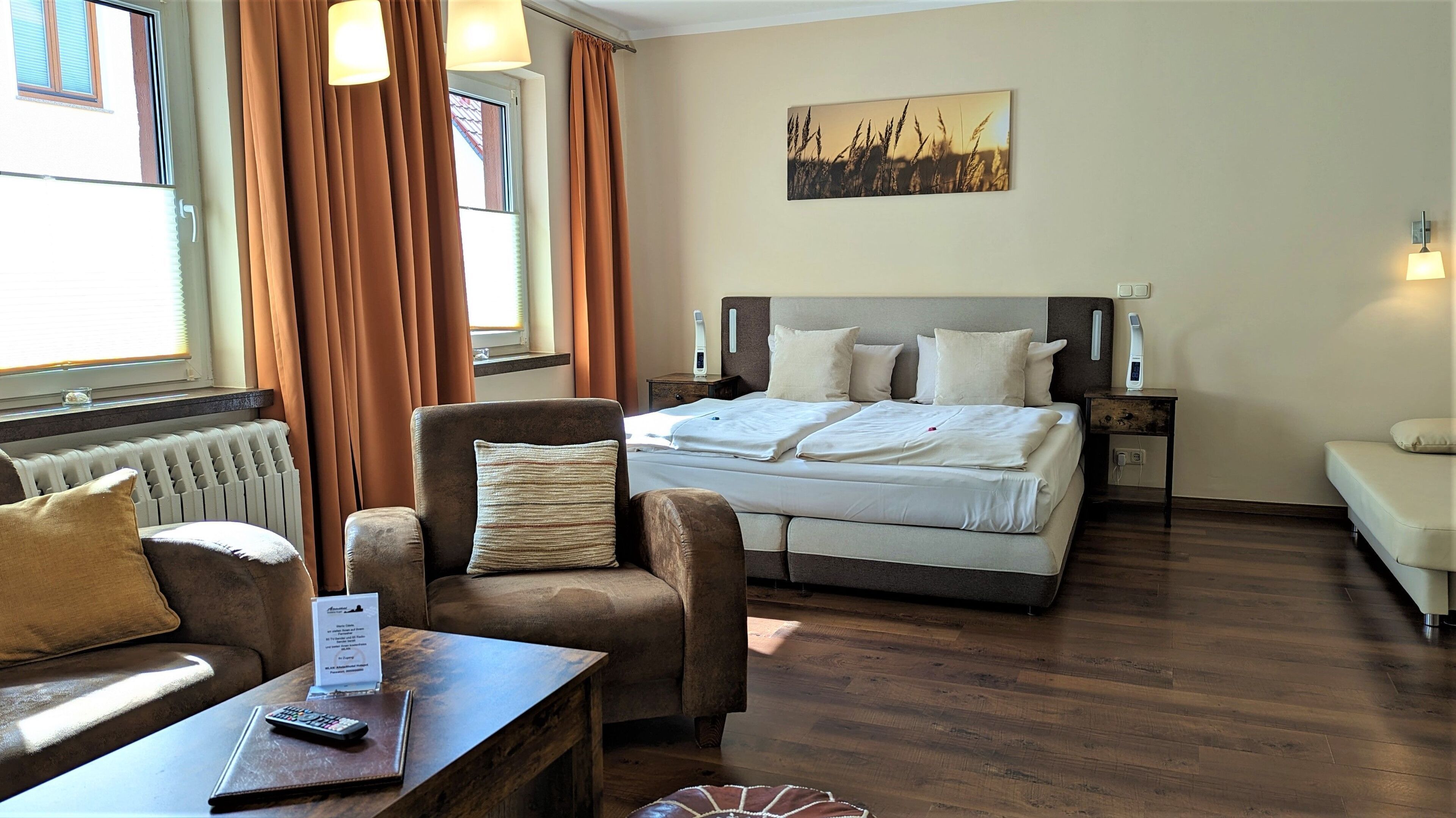 A hotel room with a bed, a chair, a sofa, a table with a remote control, and a window with curtains.