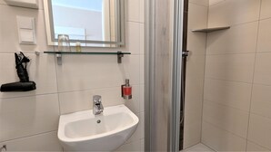 A bathroom with a white sink, a mirror above it, and a shower area. - Single room Standard - Altstadthotel Goldene Kugel Object ID 124185 (Waren (Müritz))