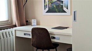 A white desk with a brown chair, a framed picture on the wall, and a sign on the desk. - Single room Standard - Altstadthotel Goldene Kugel Object ID 124185 (Waren (Müritz))