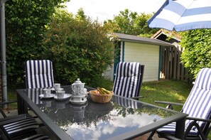 A glass table with striped chairs, a basket of fruit, and a teapot. - Ferienhaus Ankerglück (Wittmund)