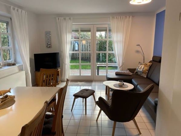 Una sala de estar con comedor, sofá, televisor y un amplio ventanal con cortinas.