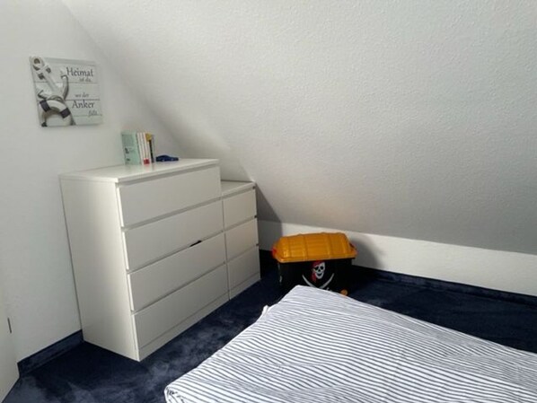 A bedroom with a bed, a white dresser, a small shelf with books, and a toy chest.