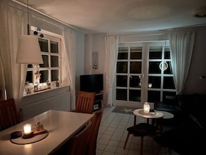 Una sala de estar con una mesa de comedor, televisor, sofá y ventana con cortinas.