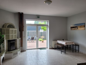 Um quarto com lareira, uma mesa com toalha florida, um banco e uma porta que dá para o exterior.