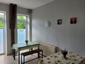 Una habitación con una mesa, un banco, dos plantas en macetas, un radiador y obras de arte en la pared.