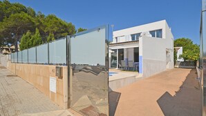A modern building with a glass facade, a paved walkway, and a clear blue sky. - DJ's House - Modern and stylish villa by the sea in Mallorca (Son Serra de Marina)
