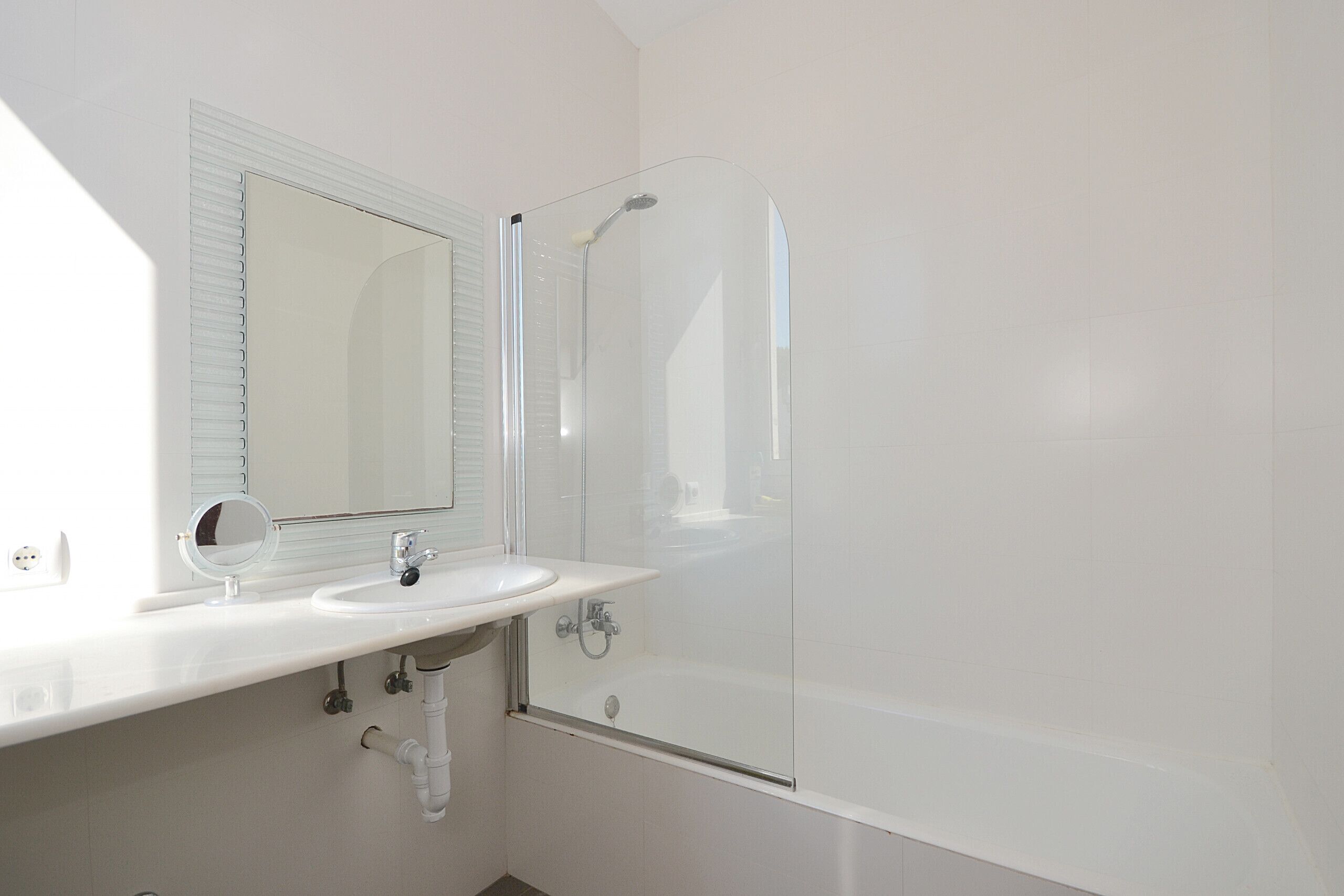 A bathroom with a sink, mirror, and glass-enclosed shower.