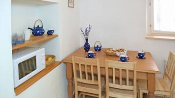 Ein Essbereich mit einem Holztisch, Stühlen, einer Mikrowelle und blauen Teekannen auf einem Regal.