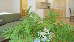 Una sala de estar con un sofá verde, una mesa de centro con una planta y una cocina al fondo.