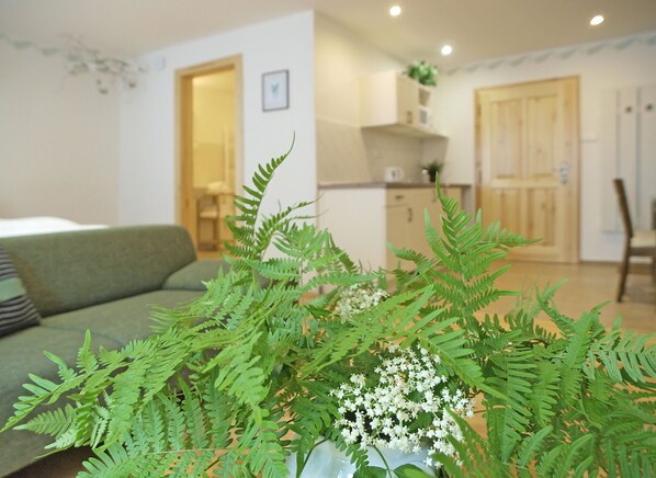 A living room with a green sofa, a coffee table with a plant, and a kitchen in the background. - Apartmány Domestika (Cesky Krumlov)
