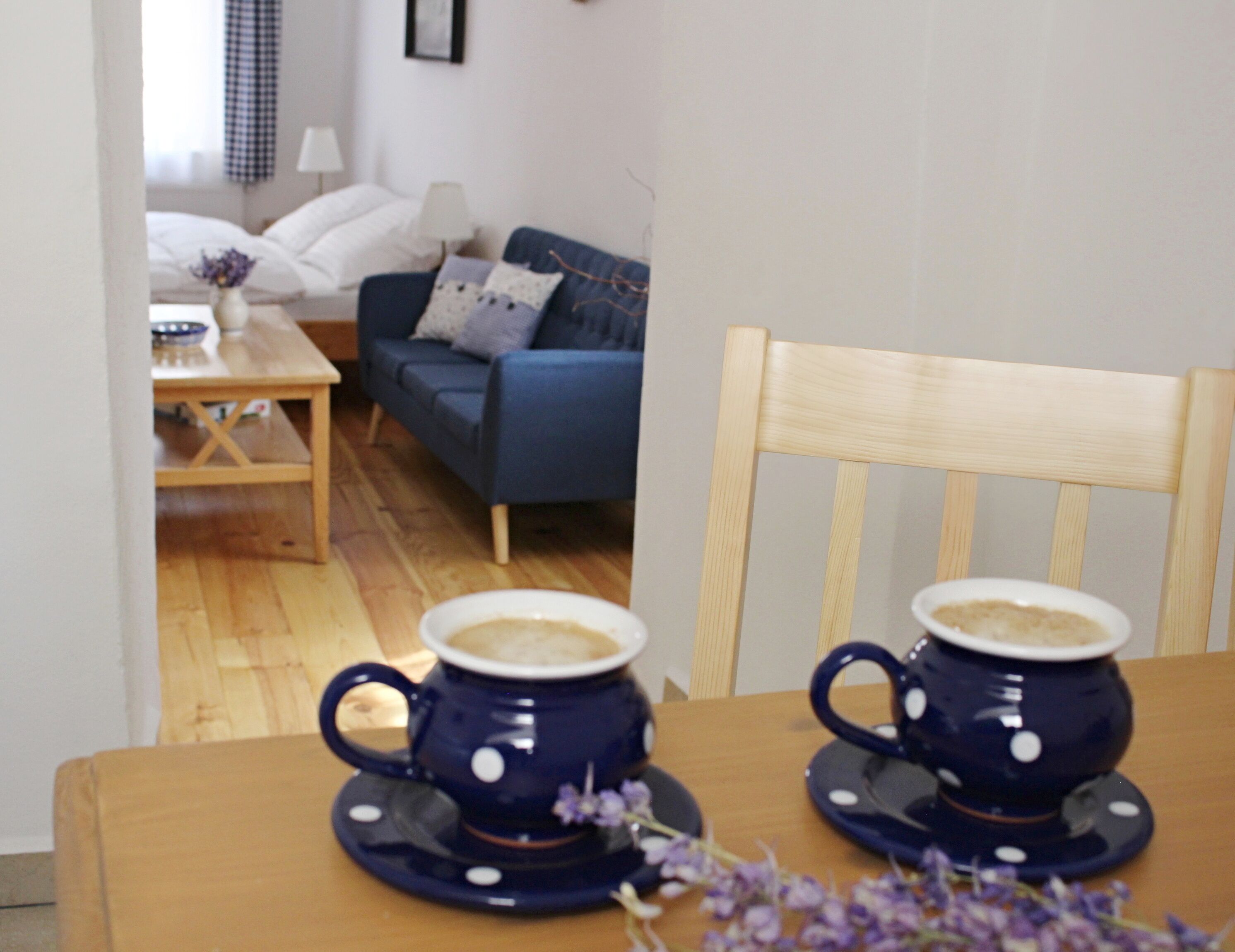 A dining table with two blue cups on saucers, a wooden chair, and a blue sofa in the background.