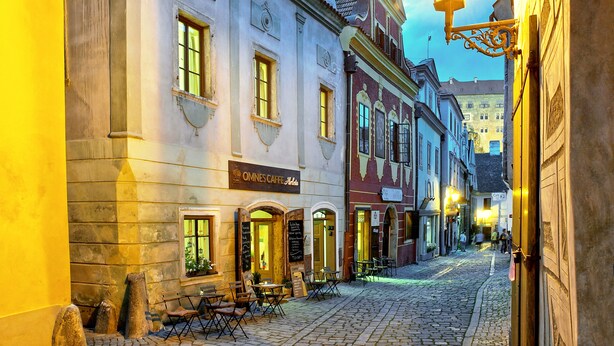 Calle empedrada con edificios históricos, mesas al aire libre y un letrero que dice 'OMNES CAFFE Anla'.