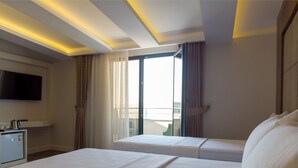 Habitación de hotel con dos camas, televisión, minibar y un amplio ventanal con cortinas.