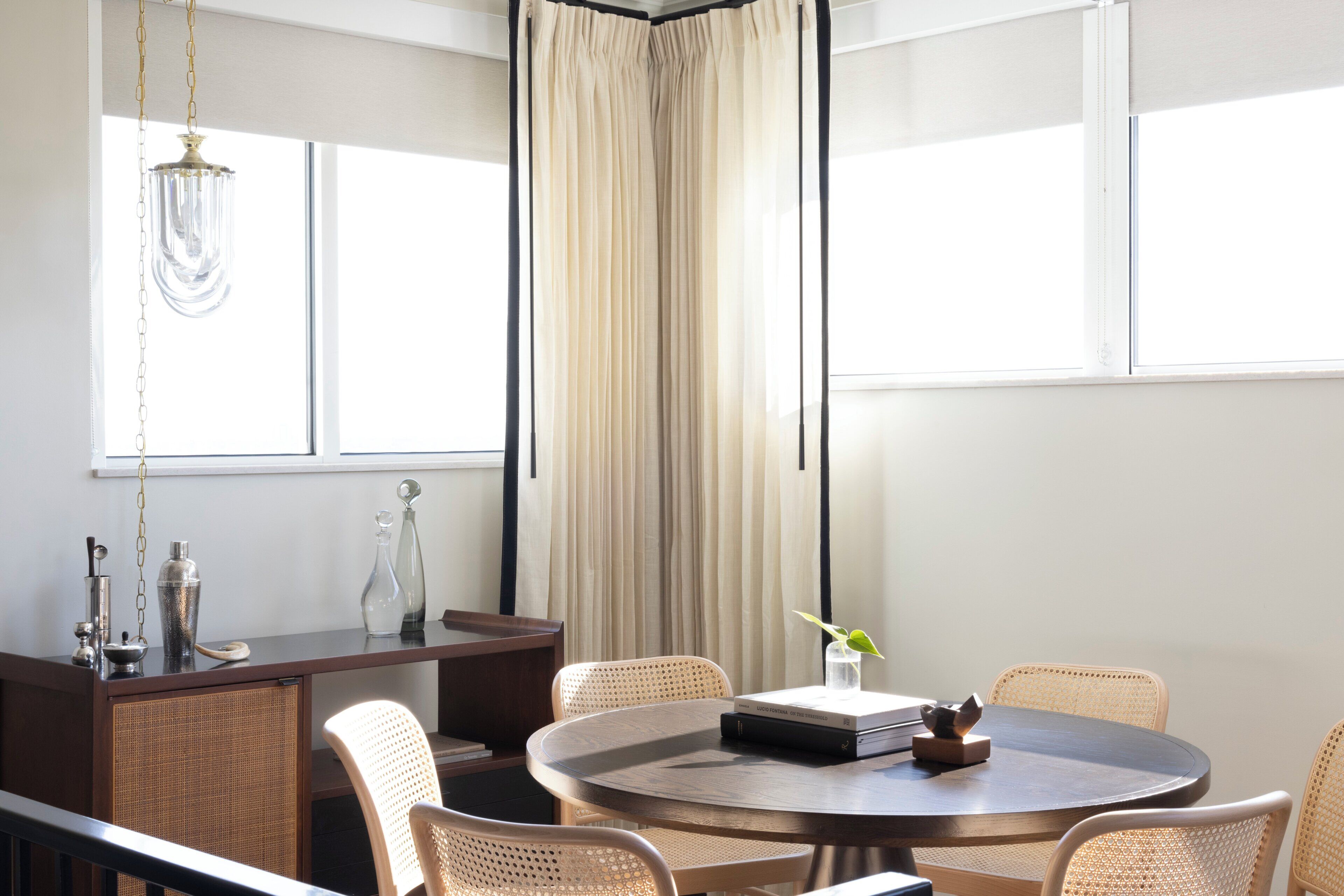Uma sala de jantar moderna com mesa redonda, cadeiras de vime e vista para o exterior.