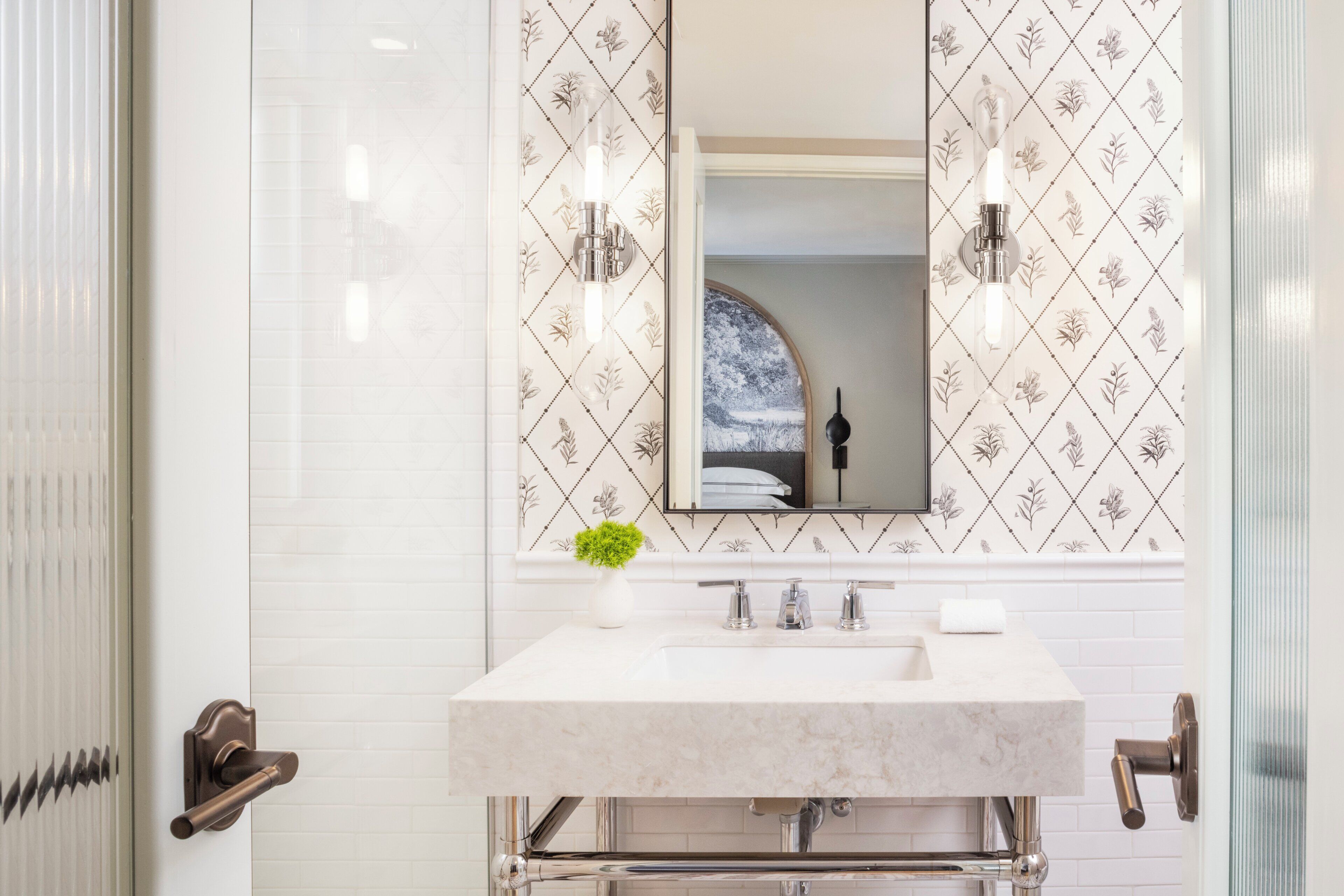 A bathroom with a white sink, two wall-mounted lights, a mirror, and a decorative wall panel.