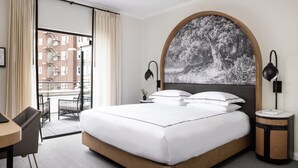 A hotel room with a large bed, a view of a building with fire escapes, a round table, and two chairs. - Kimpton Cottonwood by IHG (Omaha)