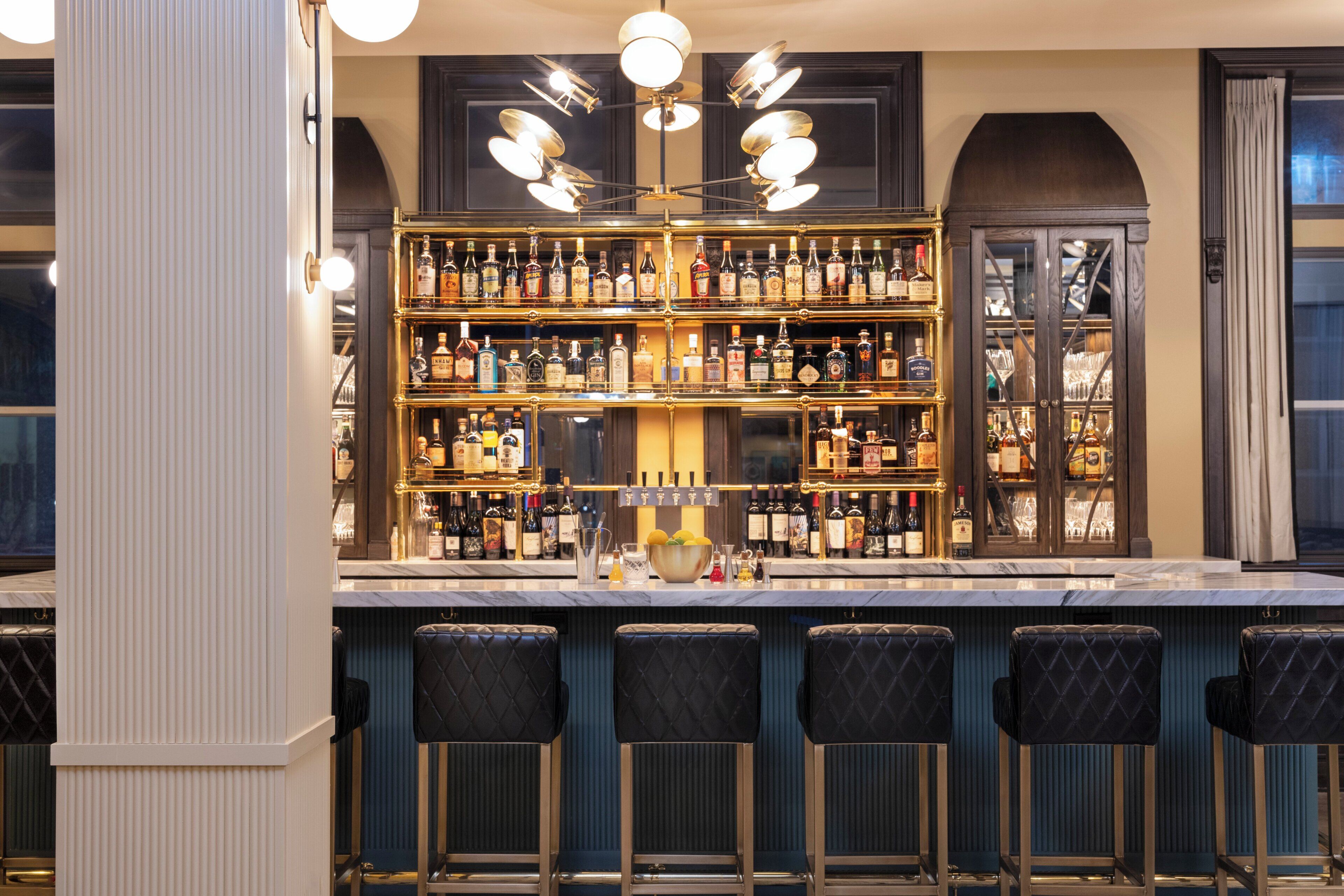 A bar area with multiple shelves of liquor bottles, a marble countertop, and bar stools.