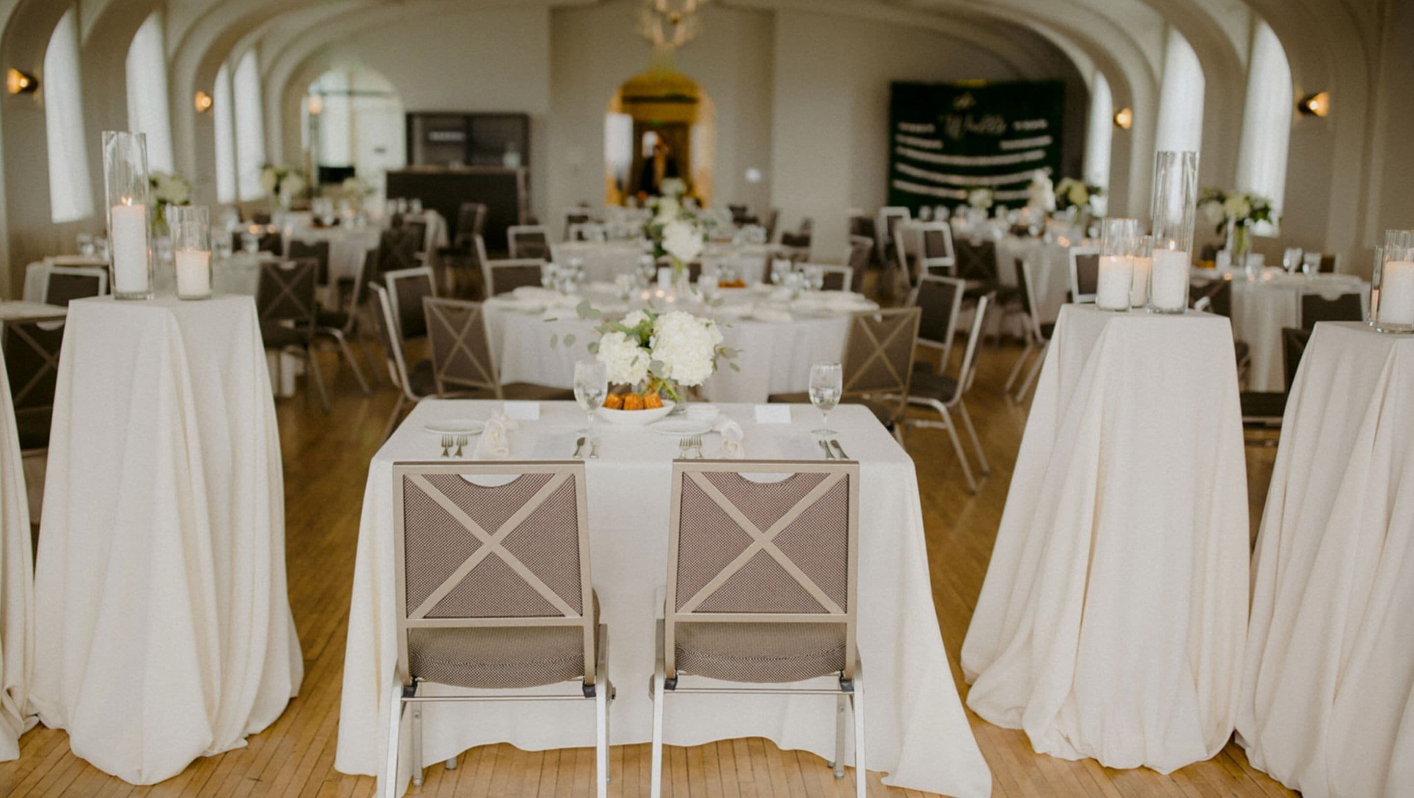 A banquet hall with round tables, white tablecloths, and chairs.