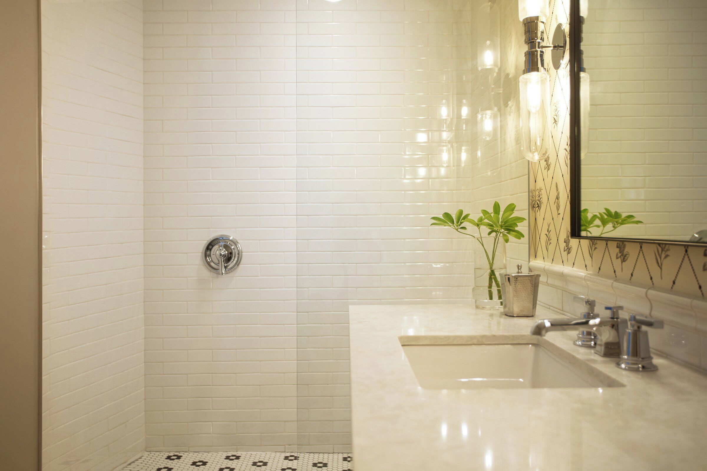A bathroom with white subway tiles, a glass shower enclosure, a sink with a mirror, and a plant on the countertop.