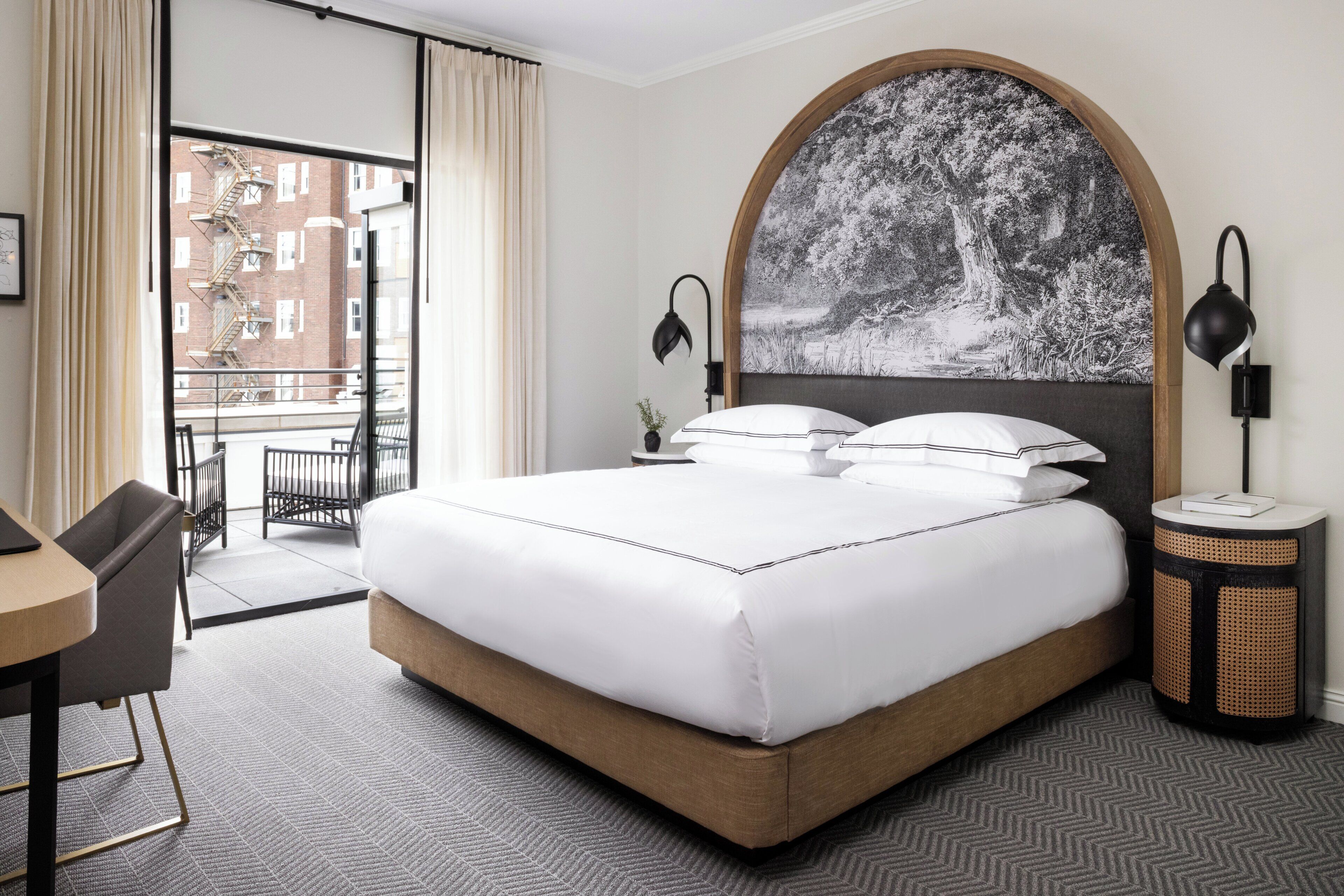 A hotel room with a large bed, a view of the city through the window, and a small table with a chair.