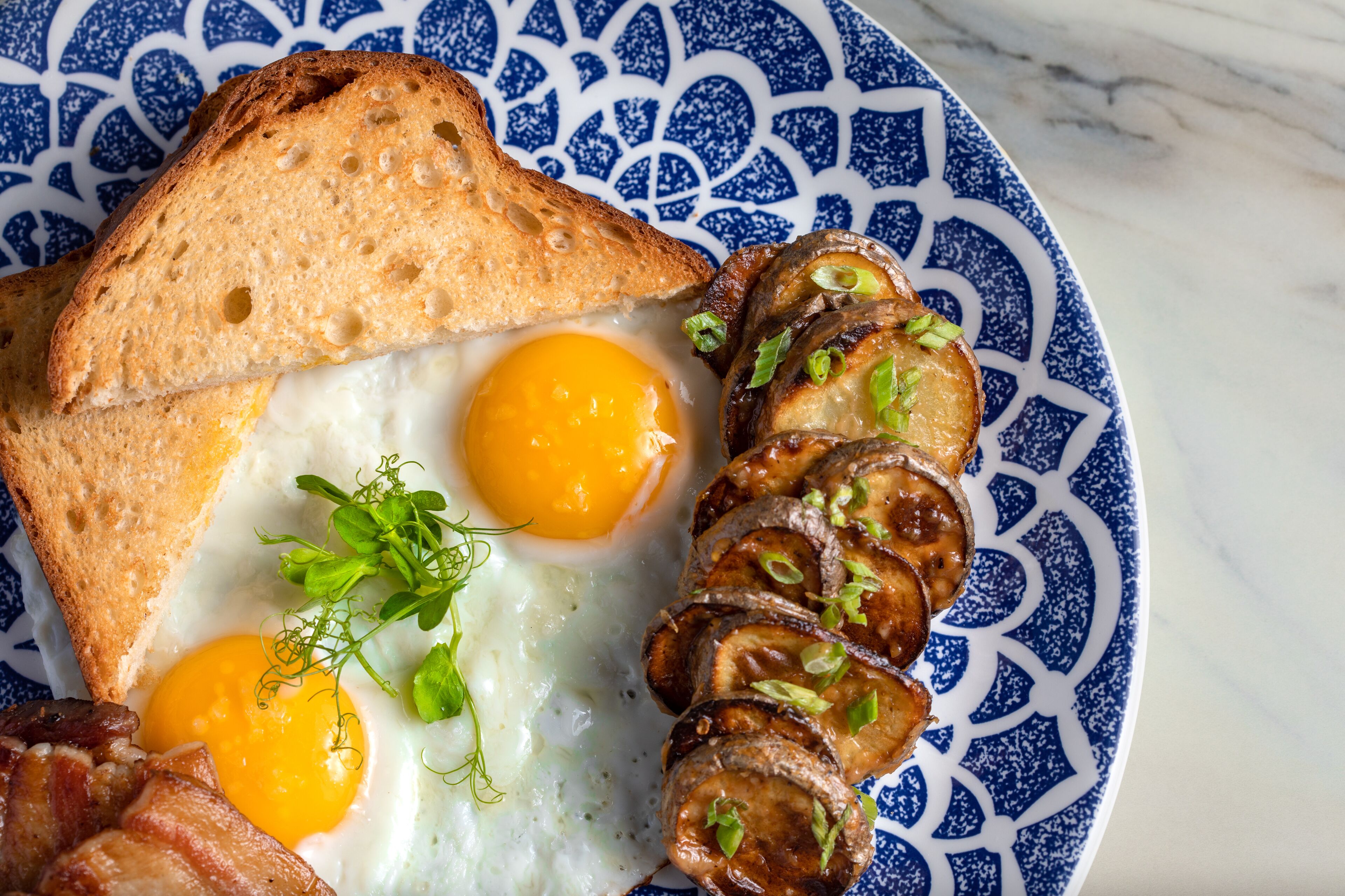 A plate with toast, two fried eggs, sliced mushrooms, and bacon.