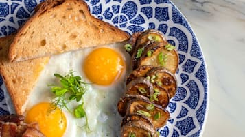 A plate with toast, two fried eggs, sliced mushrooms, and bacon.