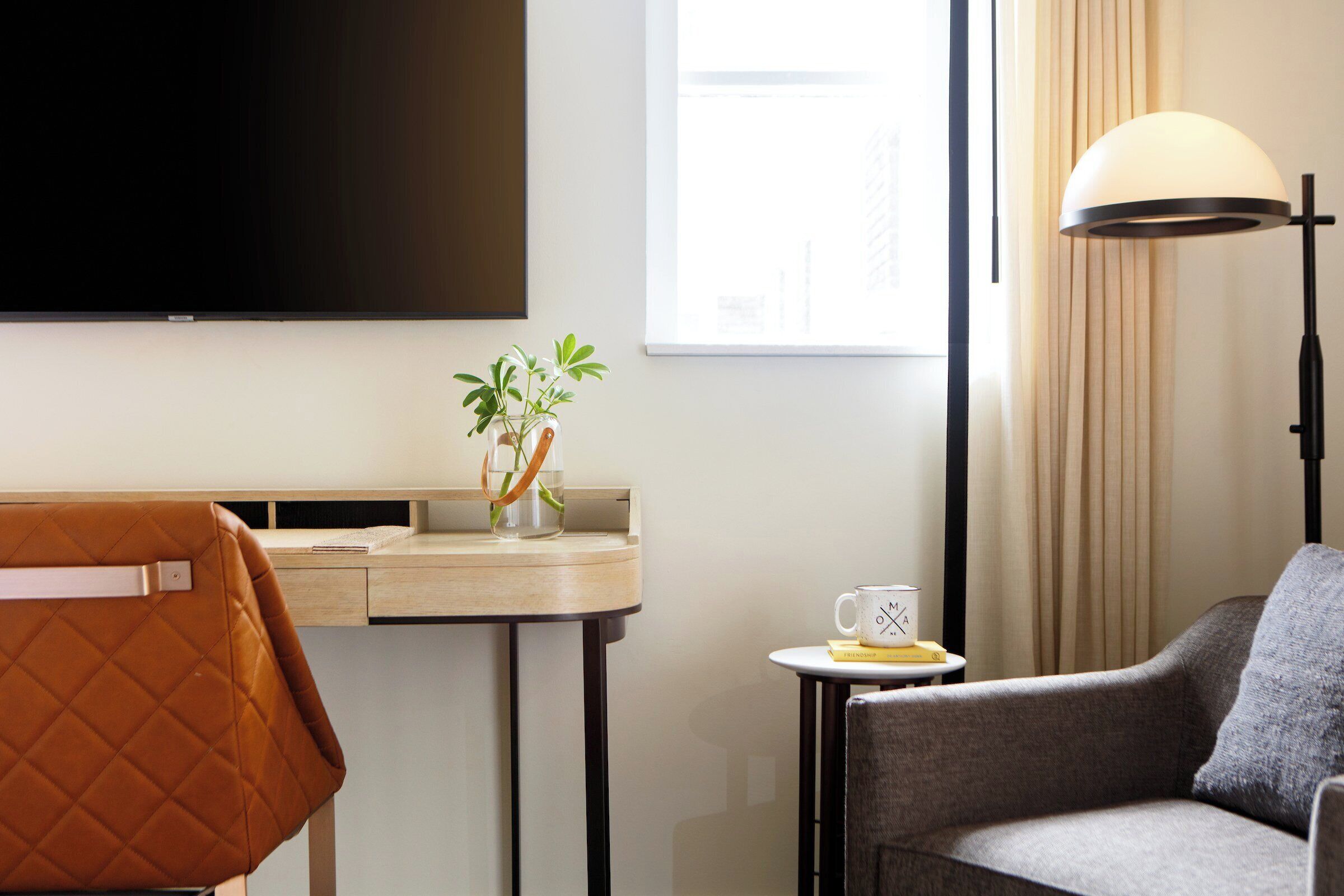 Habitación de hotel con televisor de pantalla plana, escritorio con planta, sofá y lámpara.