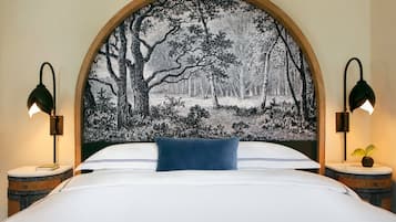 Une chambre à coucher avec un grand lit, une tête de lit ornée d’un motif représentant une forêt, deux tables de chevet avec des lampes et une petite table ronde sur laquelle est posée une plante.