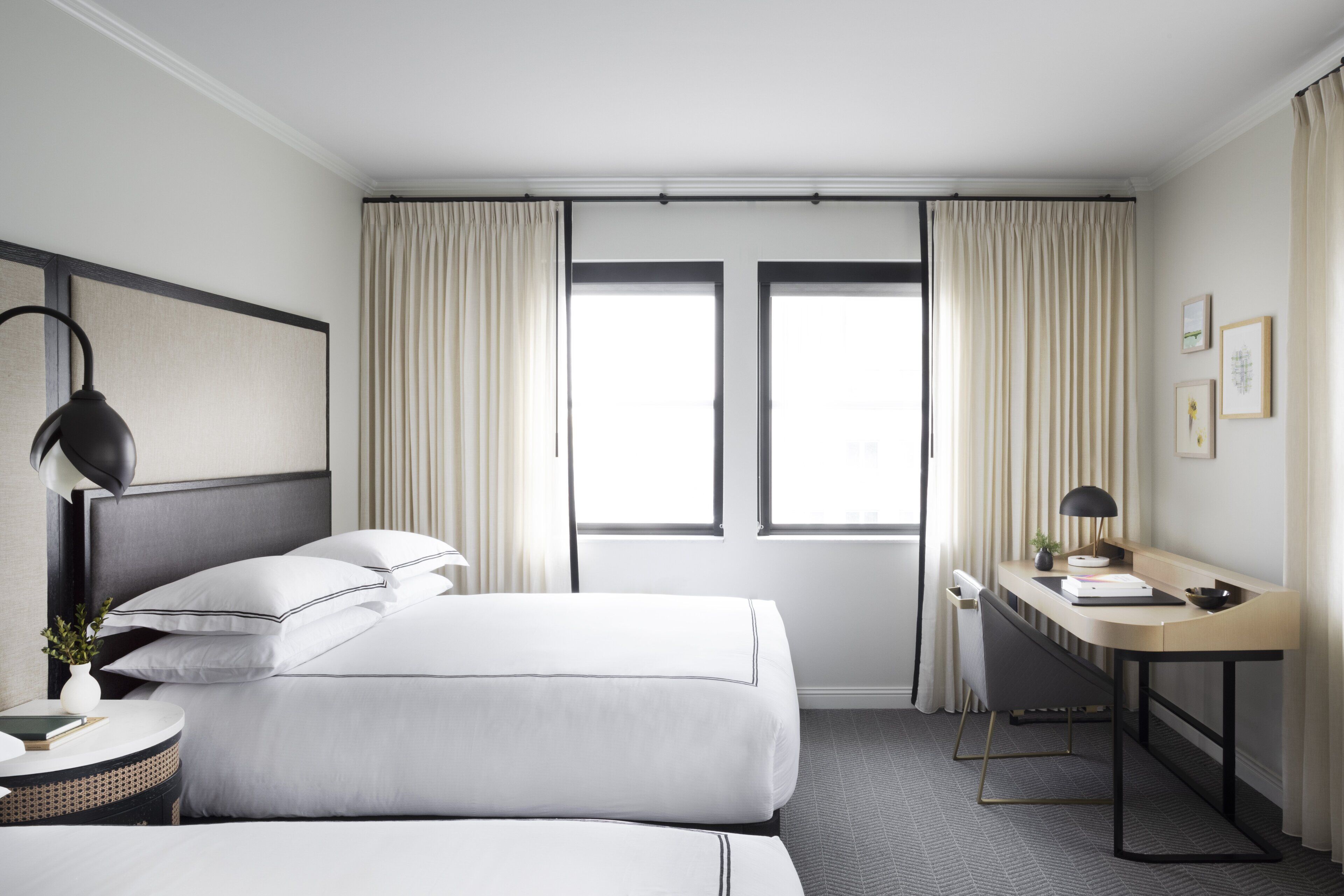 Une chambre d’hôtel avec deux lits, un bureau, une chaise, une lampe et une fenêtre avec des rideaux.