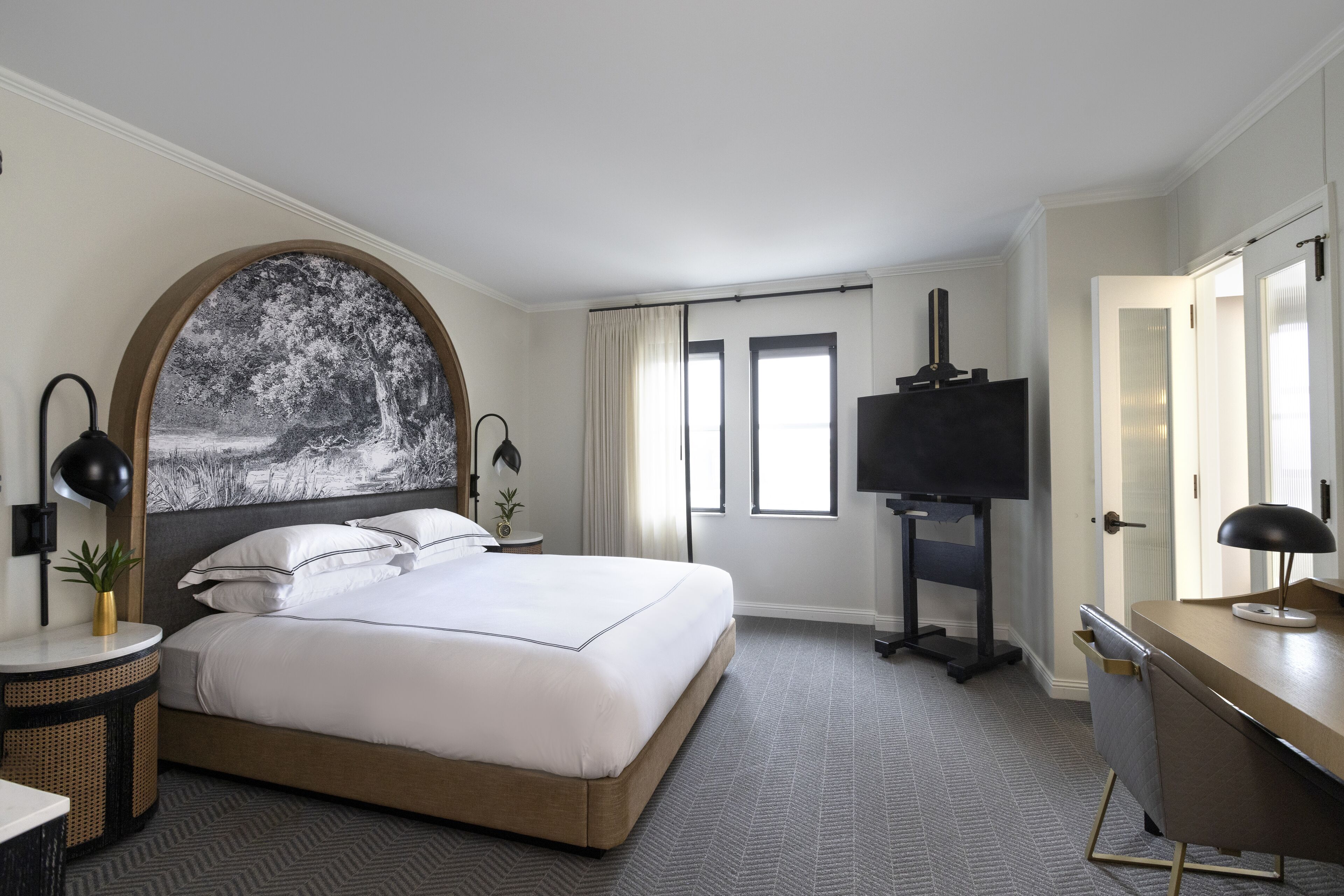 A hotel room with a large bed, a desk, a TV, and a painting on the wall.