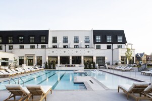 A modern hotel with a large outdoor swimming pool, sun loungers, and a well-maintained garden area.