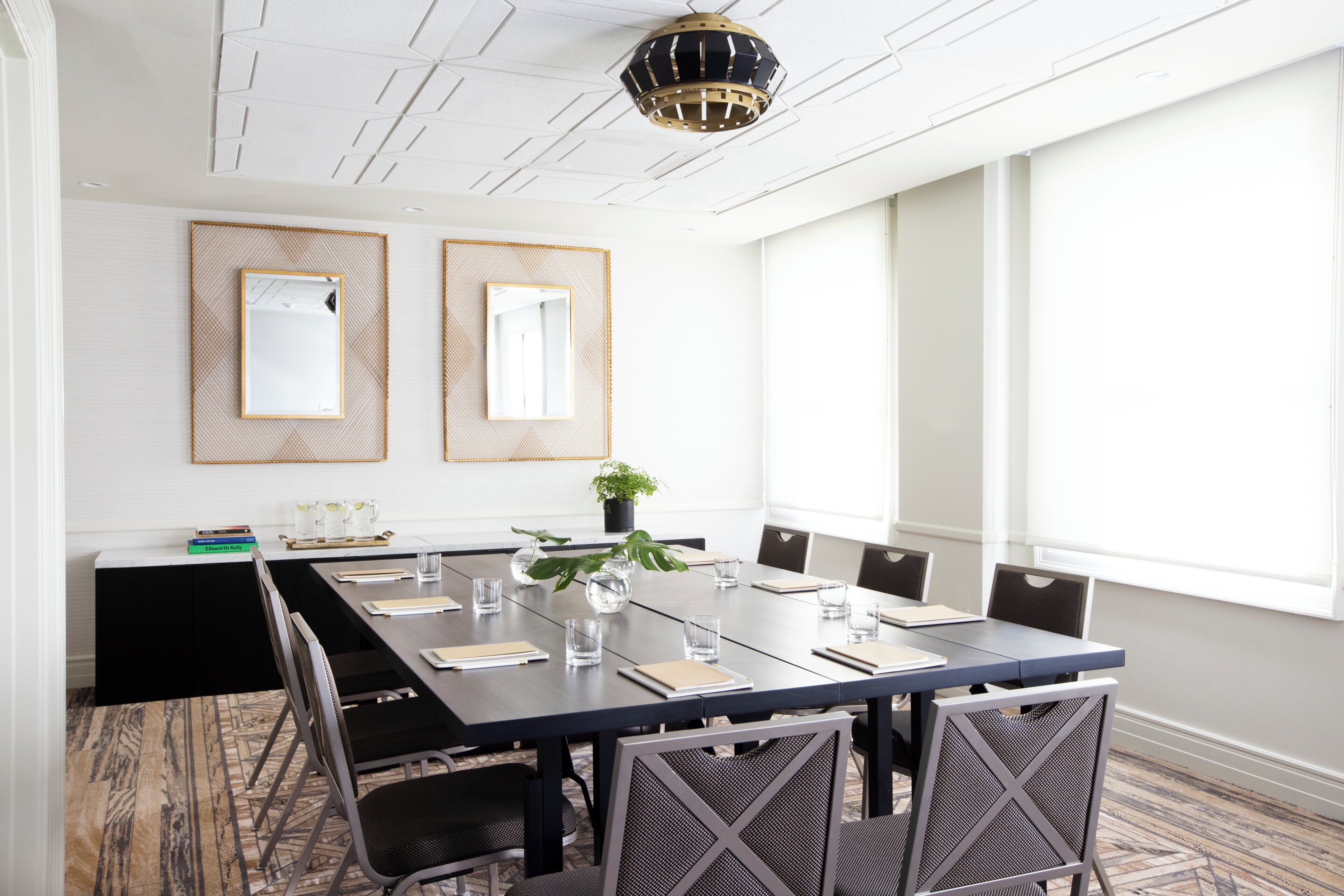 A conference room with a long table, chairs, a potted plant, and two wall mirrors.