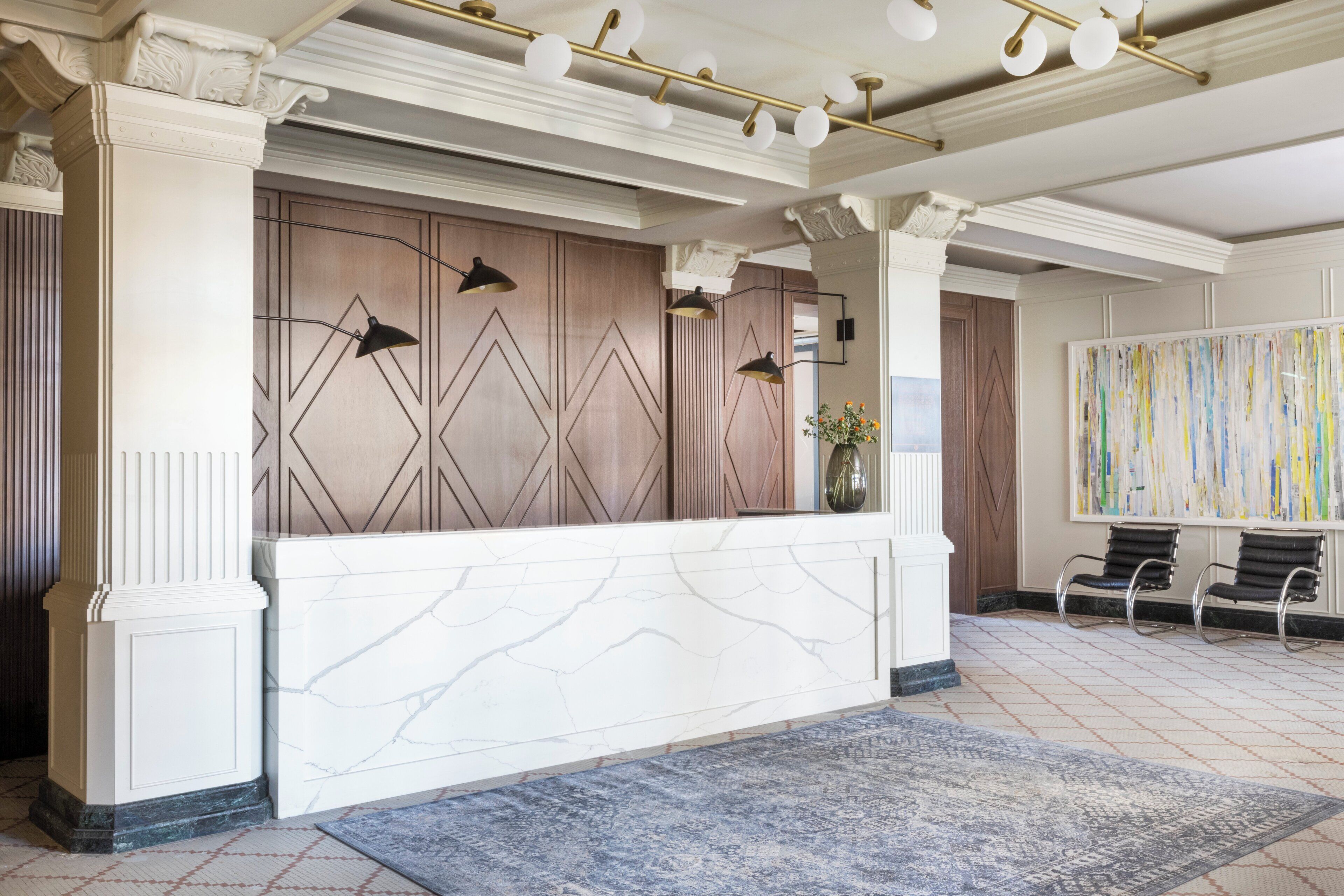 A reception area with a marble reception desk, wall-mounted lamps, a vase with flowers, and a large abstract painting.