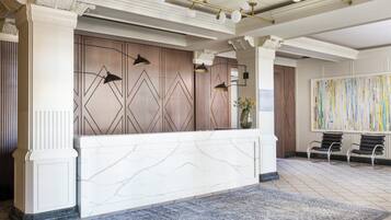 A reception area with a marble reception desk, wall-mounted lamps, a vase with flowers, and a large abstract painting.