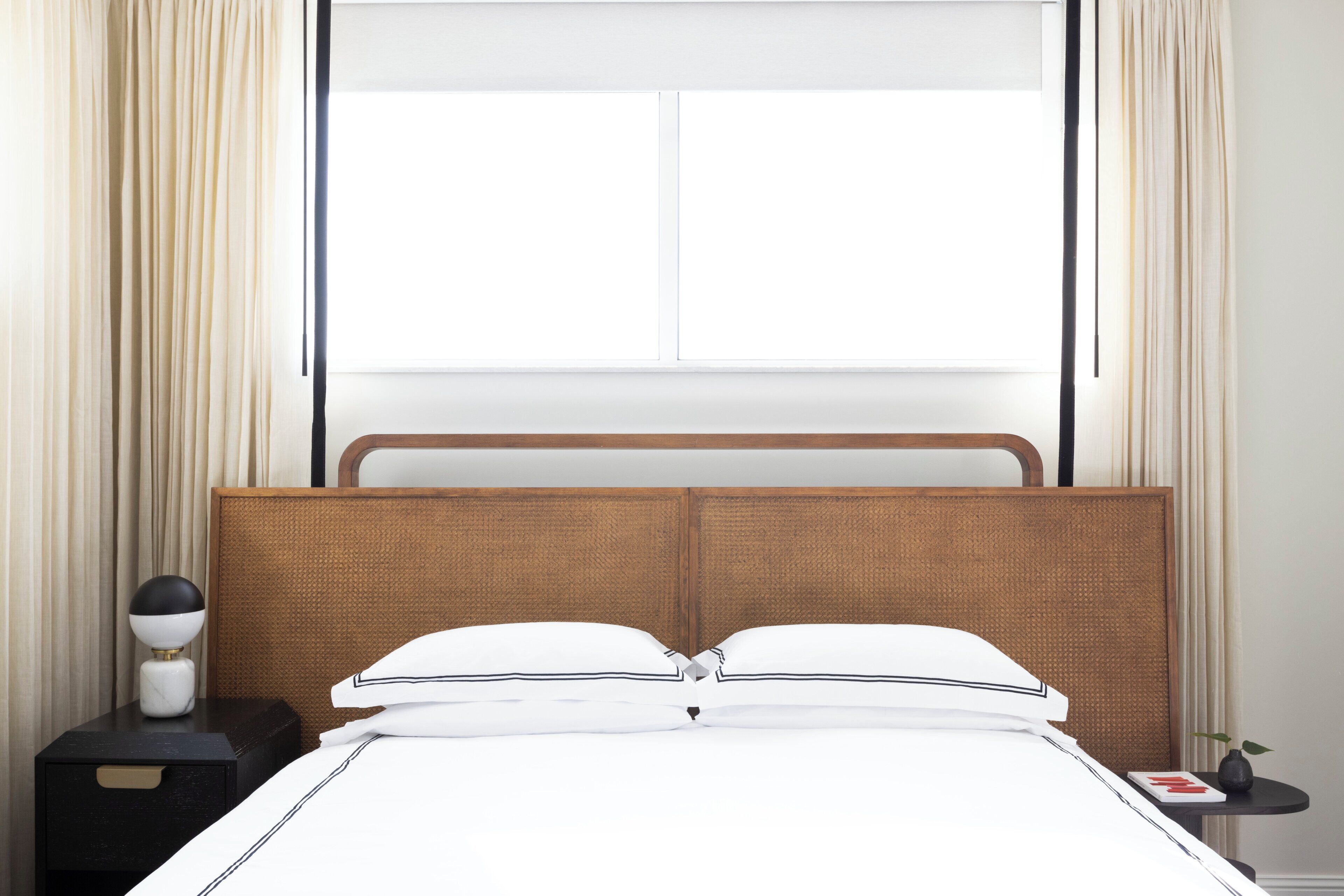 A hotel room with a bed, nightstand, lamp, and a window with curtains.