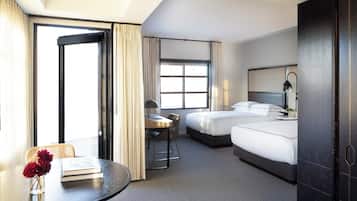 A hotel room with two beds, a dining table, a chair, and a window.