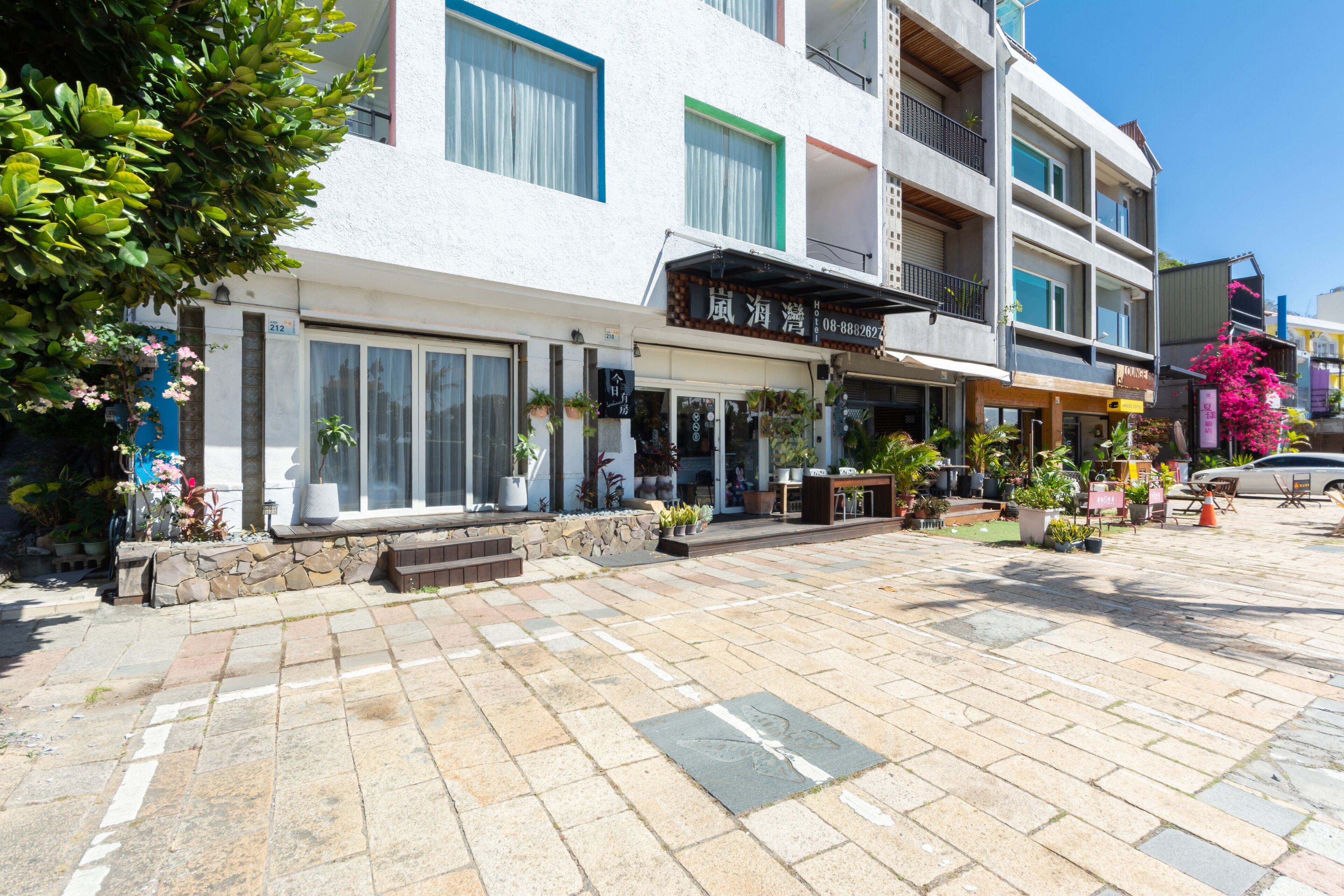 Un hôtel avec une entrée pavée de pierres, des plantes en pot et une enseigne.